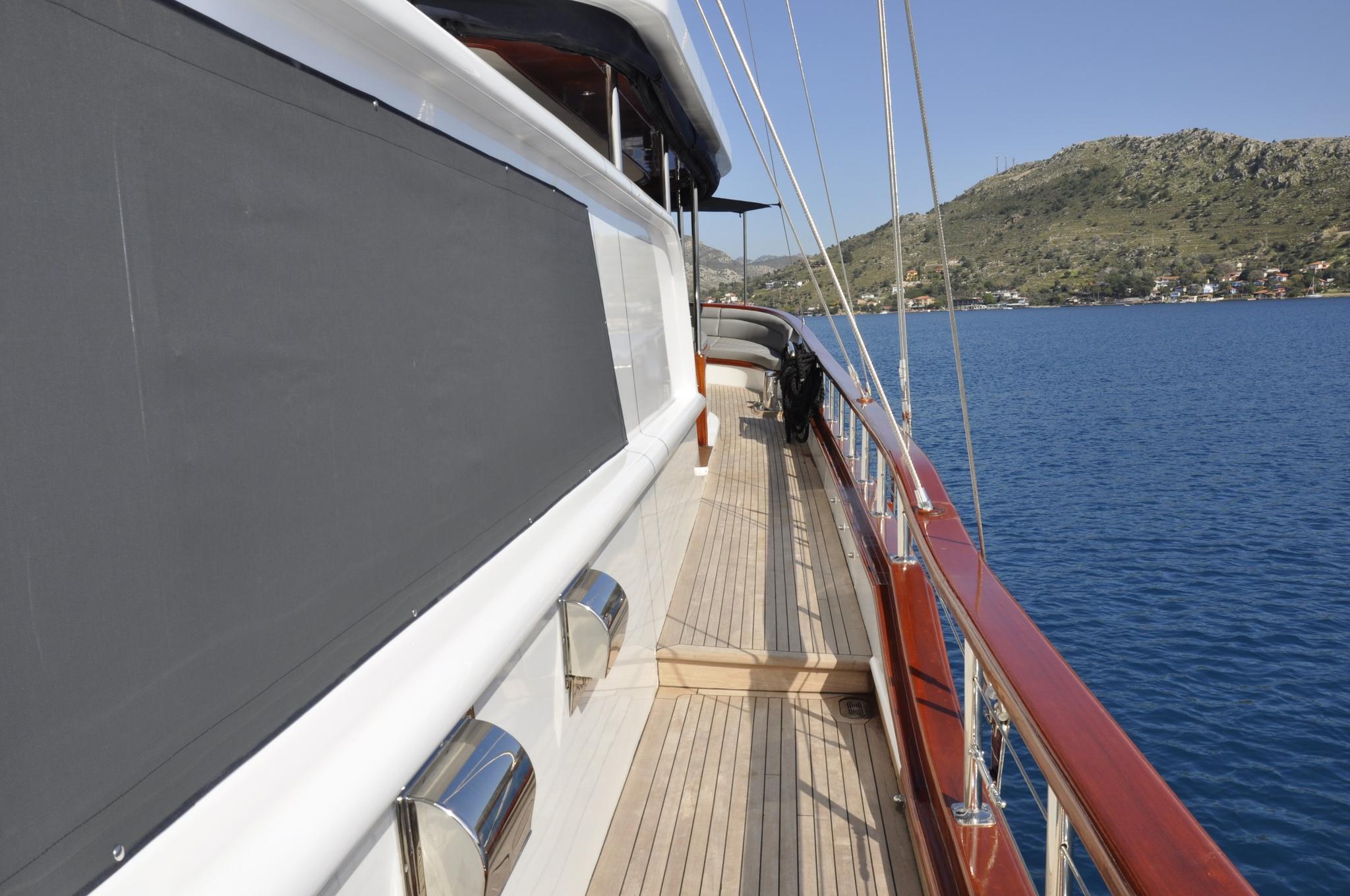 gulet side deck with teak planking, white safety railings and stainless steel stanchions overlooking blue Mediterranean waters