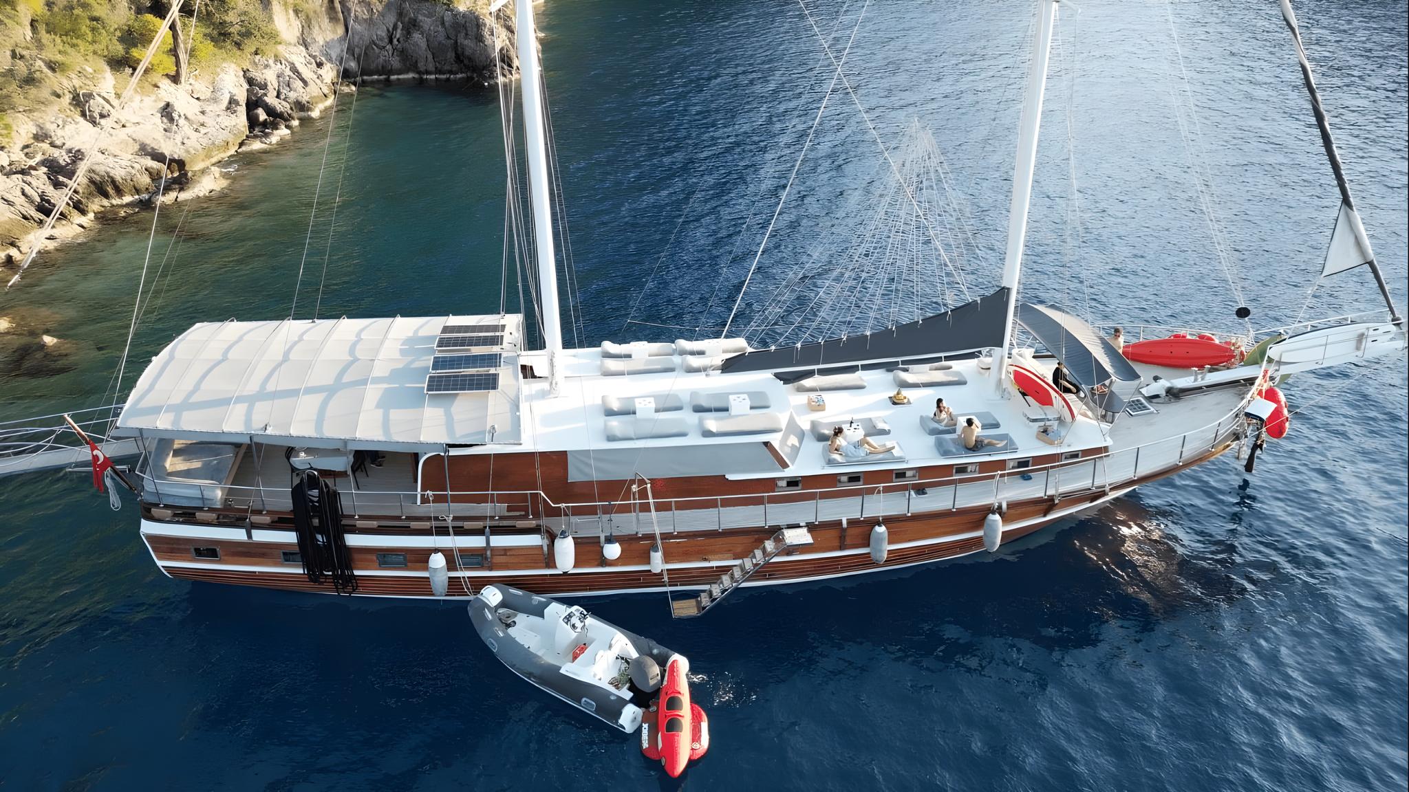 aerial view of traditional gulet yacht with white deck and wooden hull anchored in turquoise bay