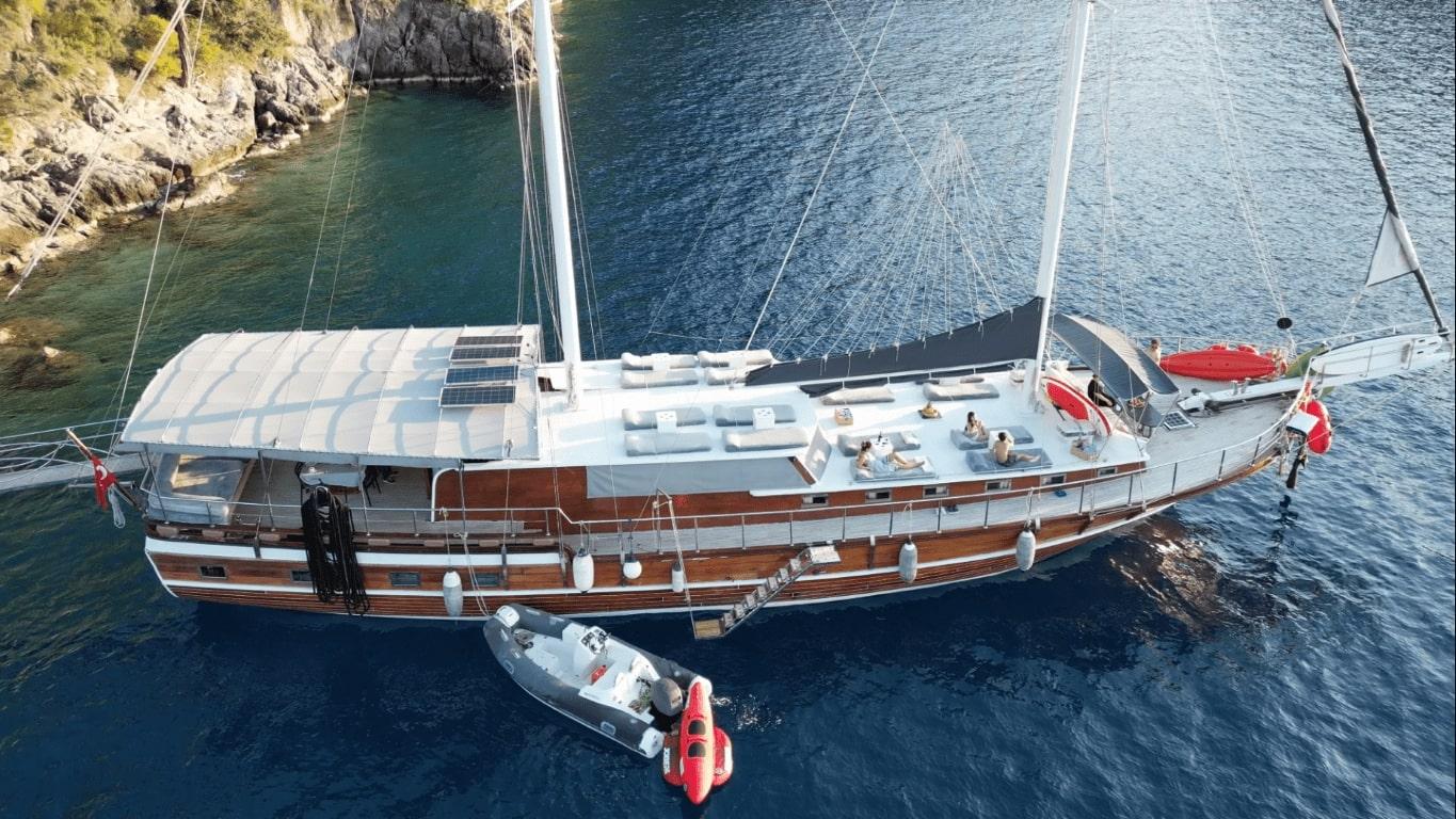 aerial view of traditional gulet yacht with white deck and wooden hull anchored in turquoise bay