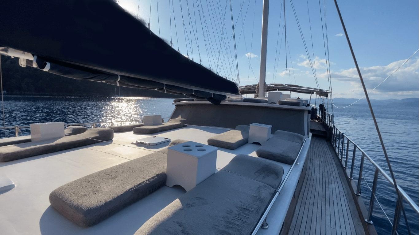 gulet forward deck with curved built-in seating, white coffee table, and teak decking