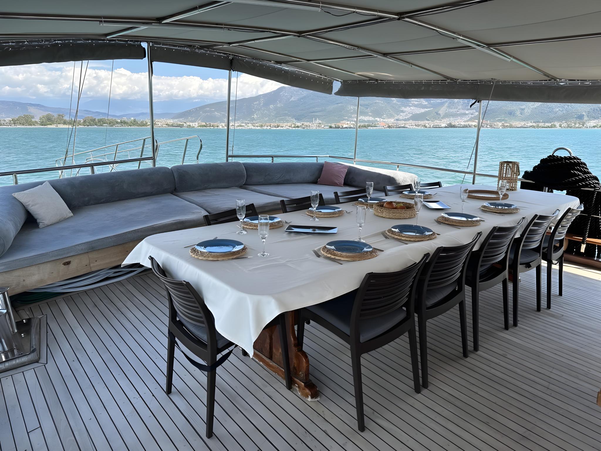 Covered aft deck dining area with white tablecloth, place settings and panoramic sea views