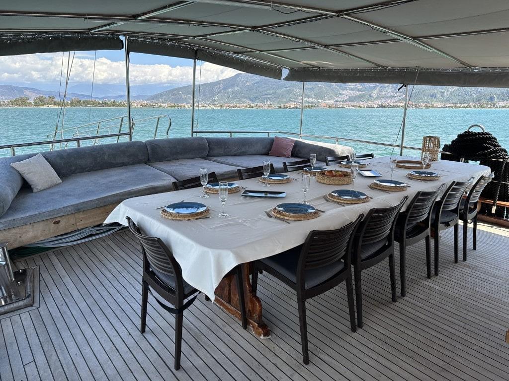 Covered aft deck dining area with white tablecloth, place settings and panoramic sea views