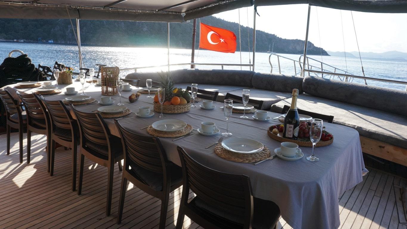 Gulet aft deck dining table set with breakfast plates, champagne bottle and Turkish flag