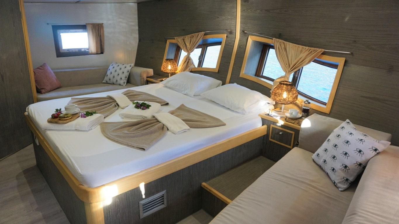 yacht guest cabin featuring double bed with decorative towels and adjacent single berth with patterned cushions