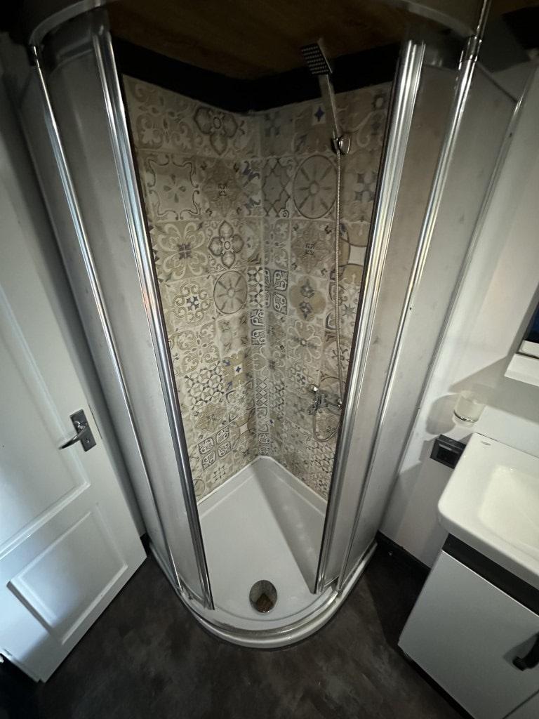 yacht bathroom featuring corner shower with decorative patterned tiles and glass doors