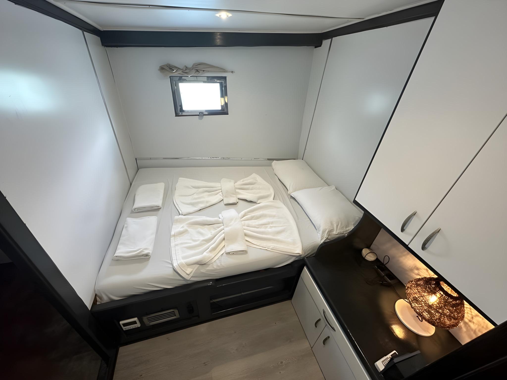 yacht cabin interior with white bedding, dark wood platform bed and porthole window