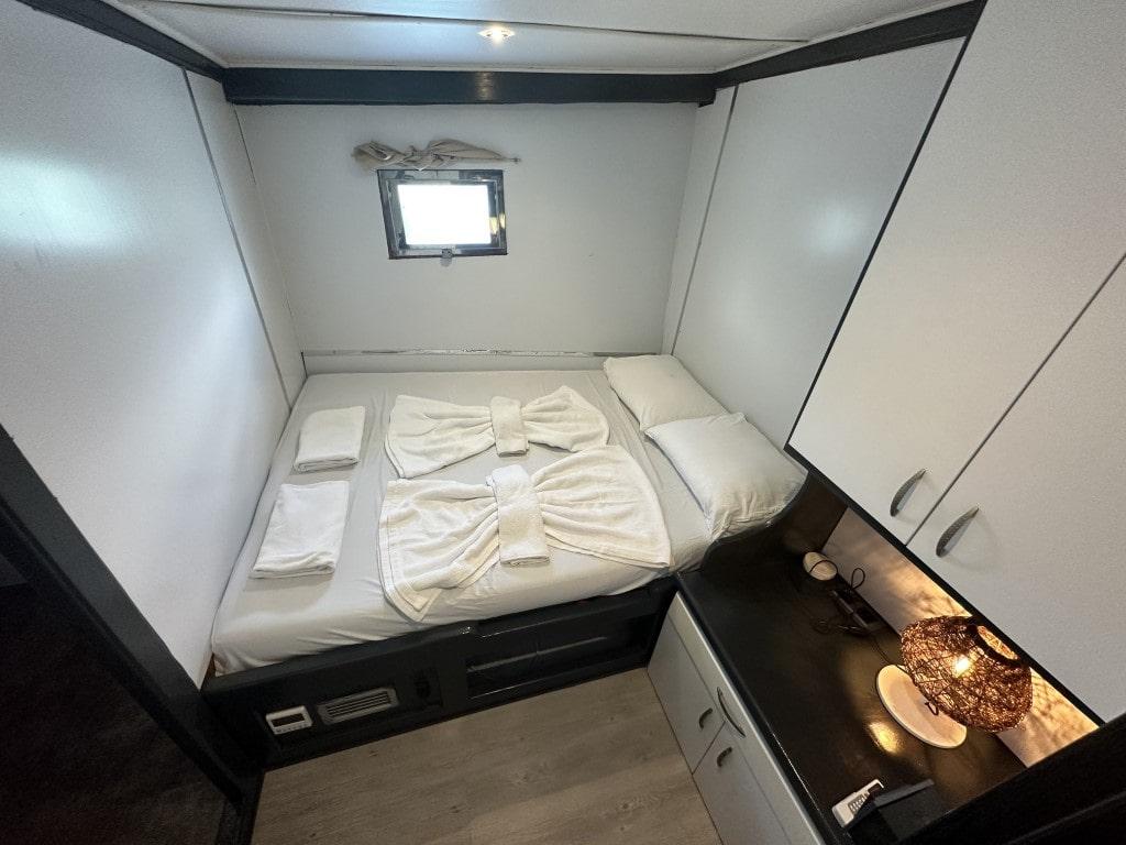 yacht cabin interior with white bedding, dark wood platform bed and porthole window