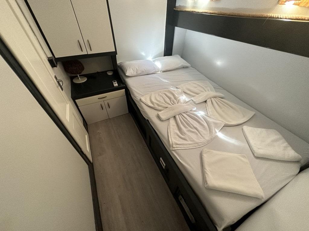 yacht guest cabin with twin beds, white linens, overhead storage cabinets and bedside table