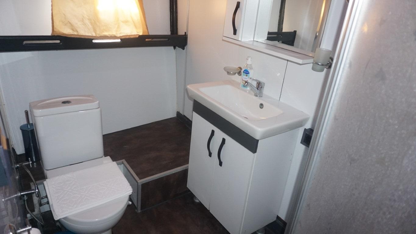 compact yacht bathroom featuring white toilet, vanity basin with mirror and dark wood flooring