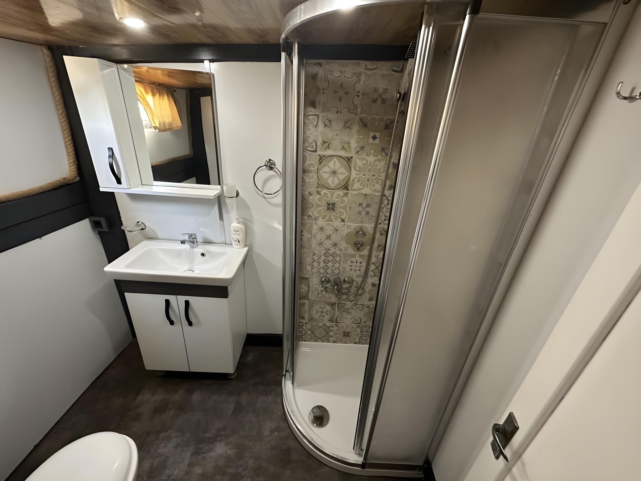 yacht bathroom with curved glass shower enclosure, white vanity unit and decorative tile backing