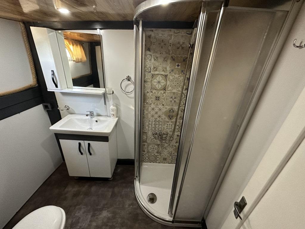 yacht bathroom with curved glass shower enclosure, white vanity unit and decorative tile backing