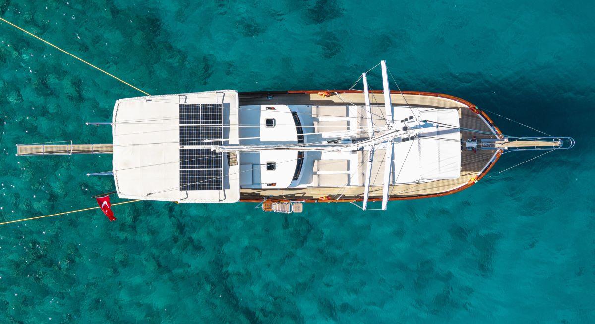 aerial view of white gulet yacht with solar panels anchored in crystal clear turquoise water