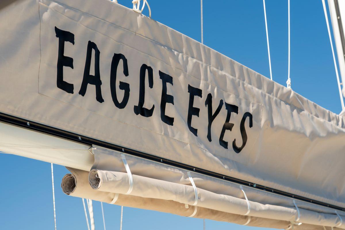 White mainsail displaying EAGLE EYES yacht name in black letters against blue sky