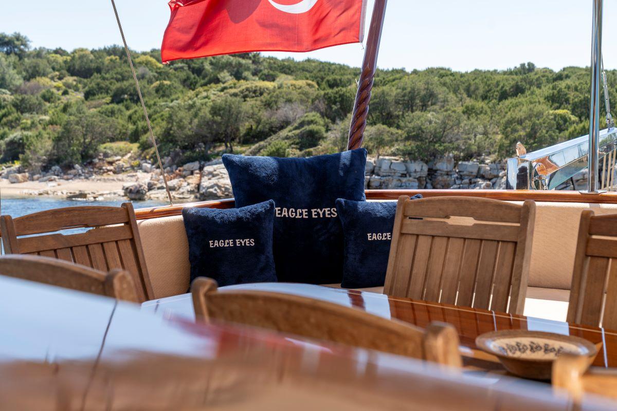 Gulet aft deck dining table with Eagle Eyes branded navy cushions and Turkish flag