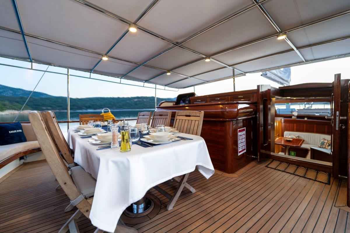Covered aft deck dining area with white tablecloth and formal place settings on luxury gulet