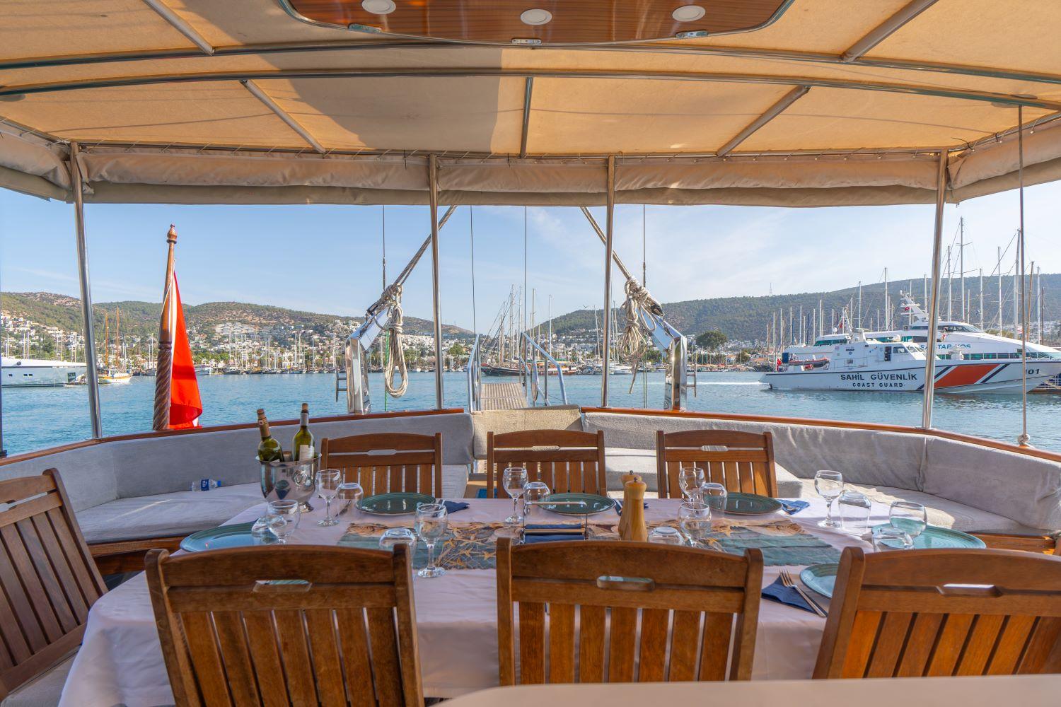 aft deck dining table set for meal with teak chairs overlooking Turkish harbor
