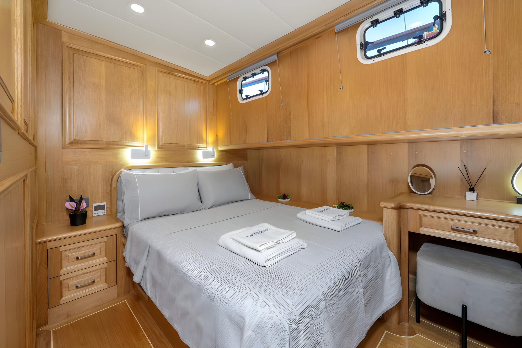 yacht guest cabin featuring double bed with grey linens, wooden paneling, built-in nightstands and portholes