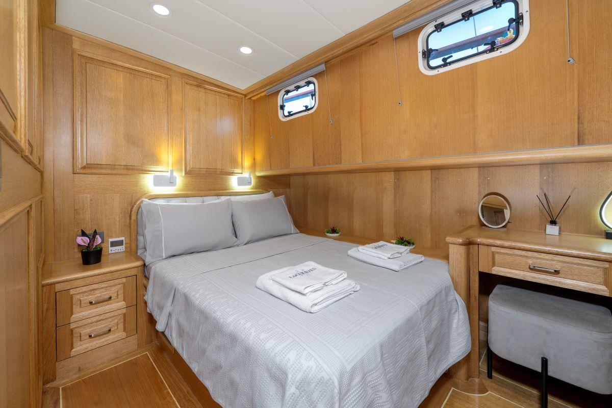 yacht guest cabin featuring double bed with grey linens, wooden paneling, built-in nightstands and portholes