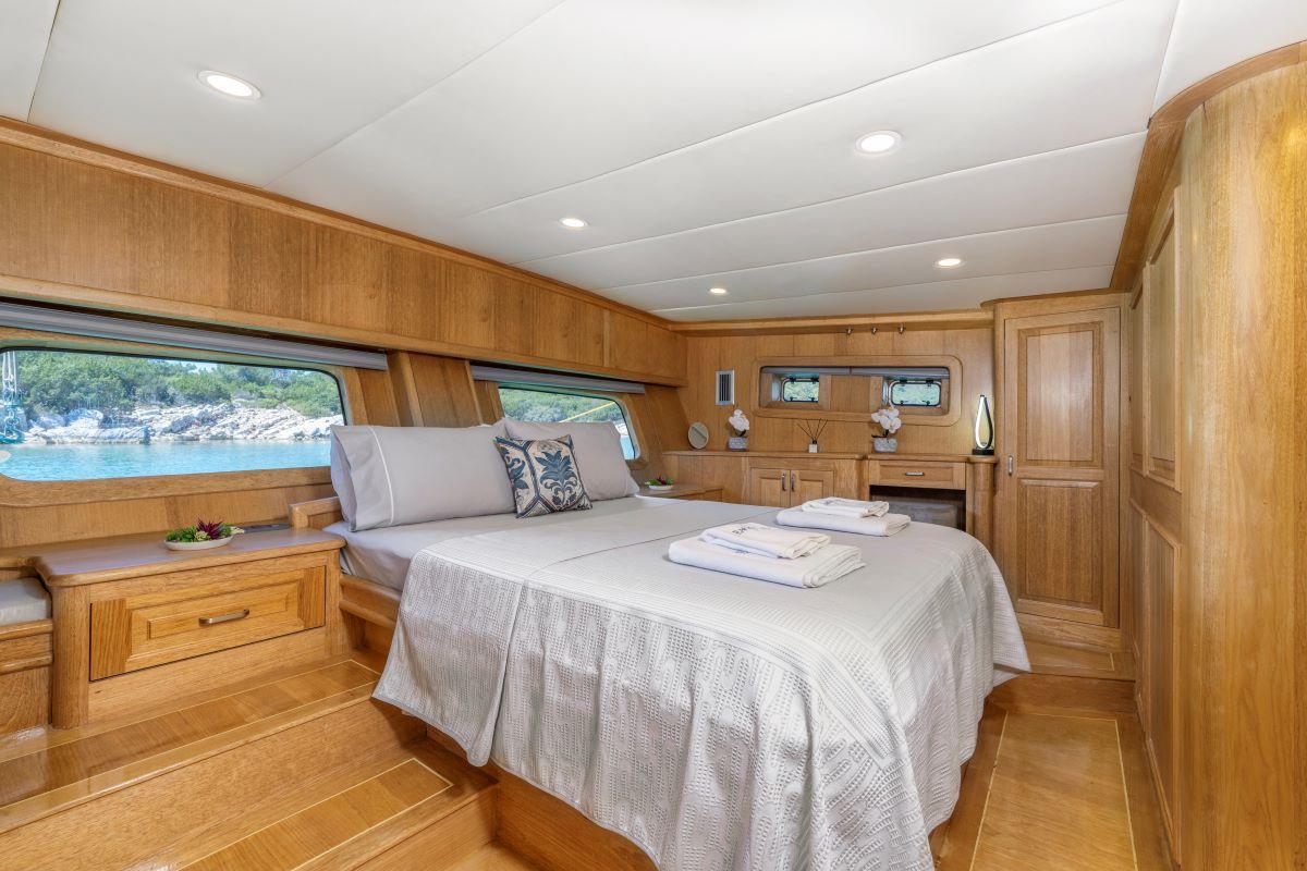 yacht cabin interior with double bed, wooden paneling, side windows showing coastline view