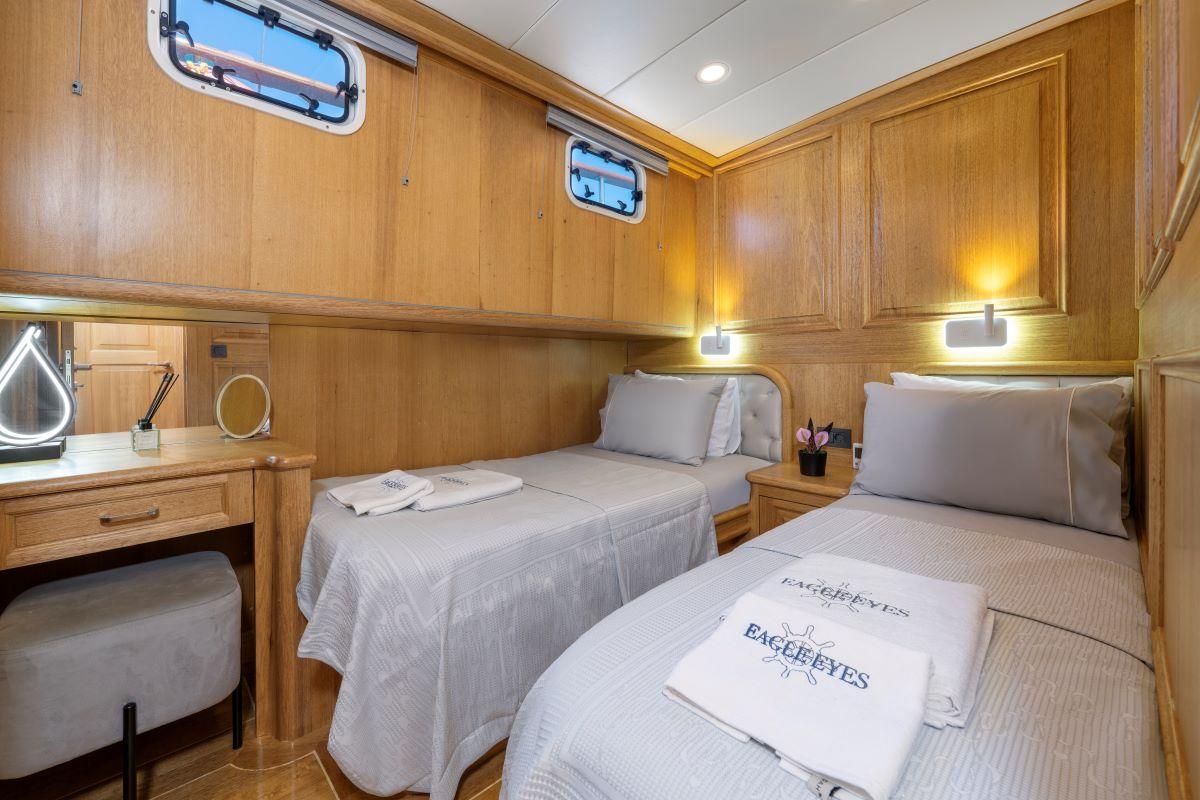 yacht twin cabin with two single beds, built-in writing desk, portholes and wood paneling