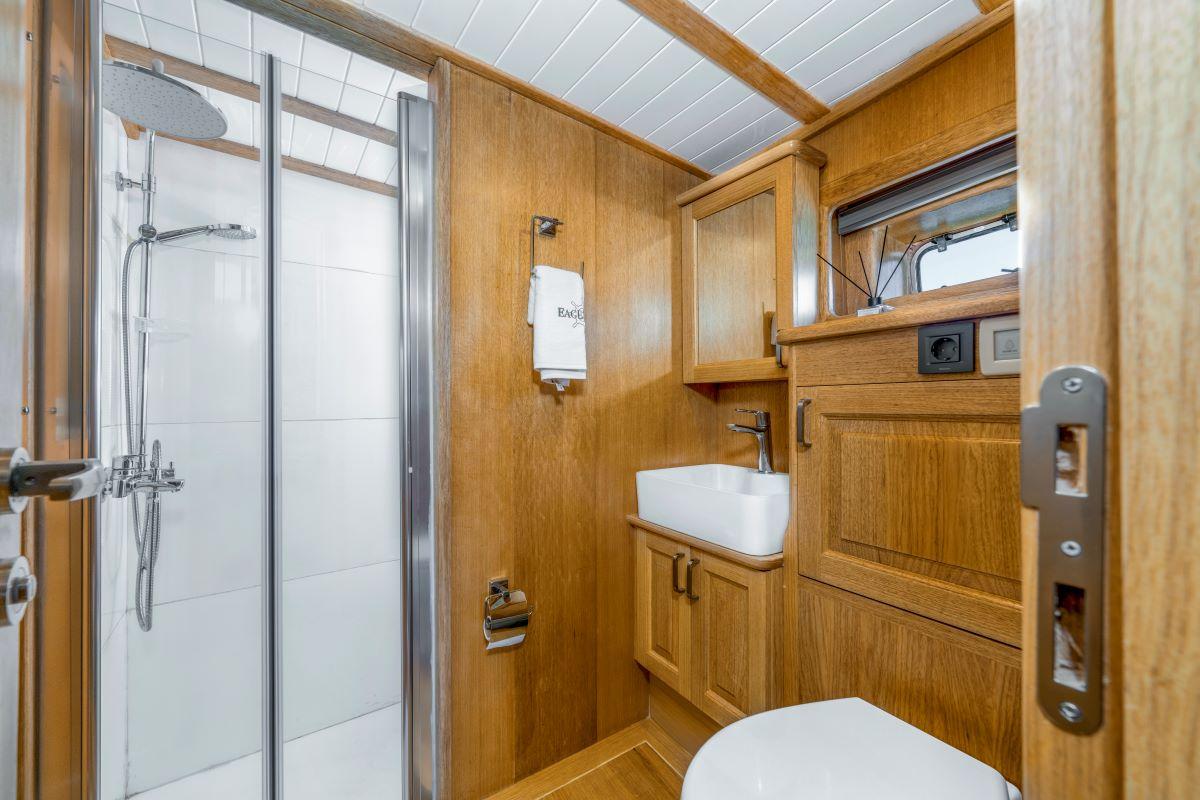 yacht bathroom featuring glass shower enclosure, white vessel sink, and warm wood paneling