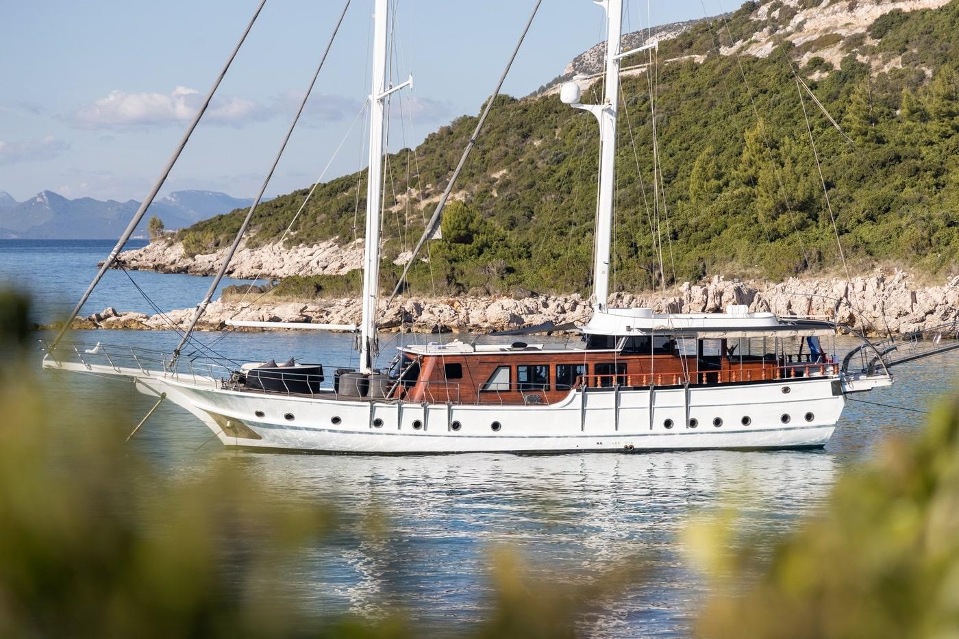 White traditional gulet yacht anchored in scenic Mediterranean bay with forested coastline