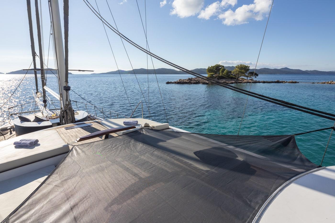 Sailing yacht foredeck with gray sail and rigging in turquoise waters