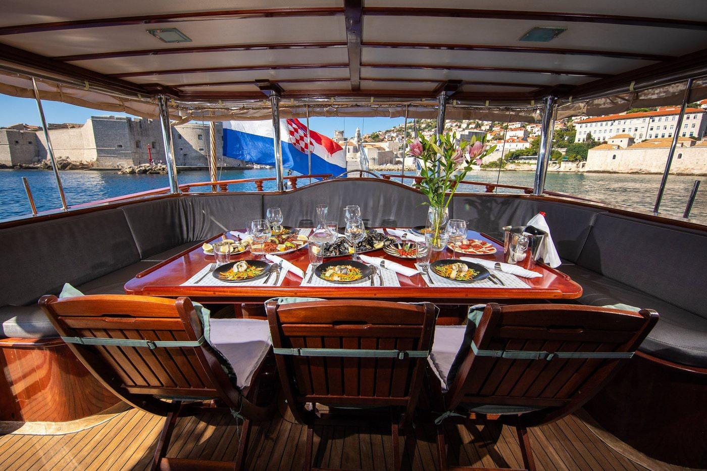 Gulet yacht aft deck dining table set for meal with Croatian harbor view