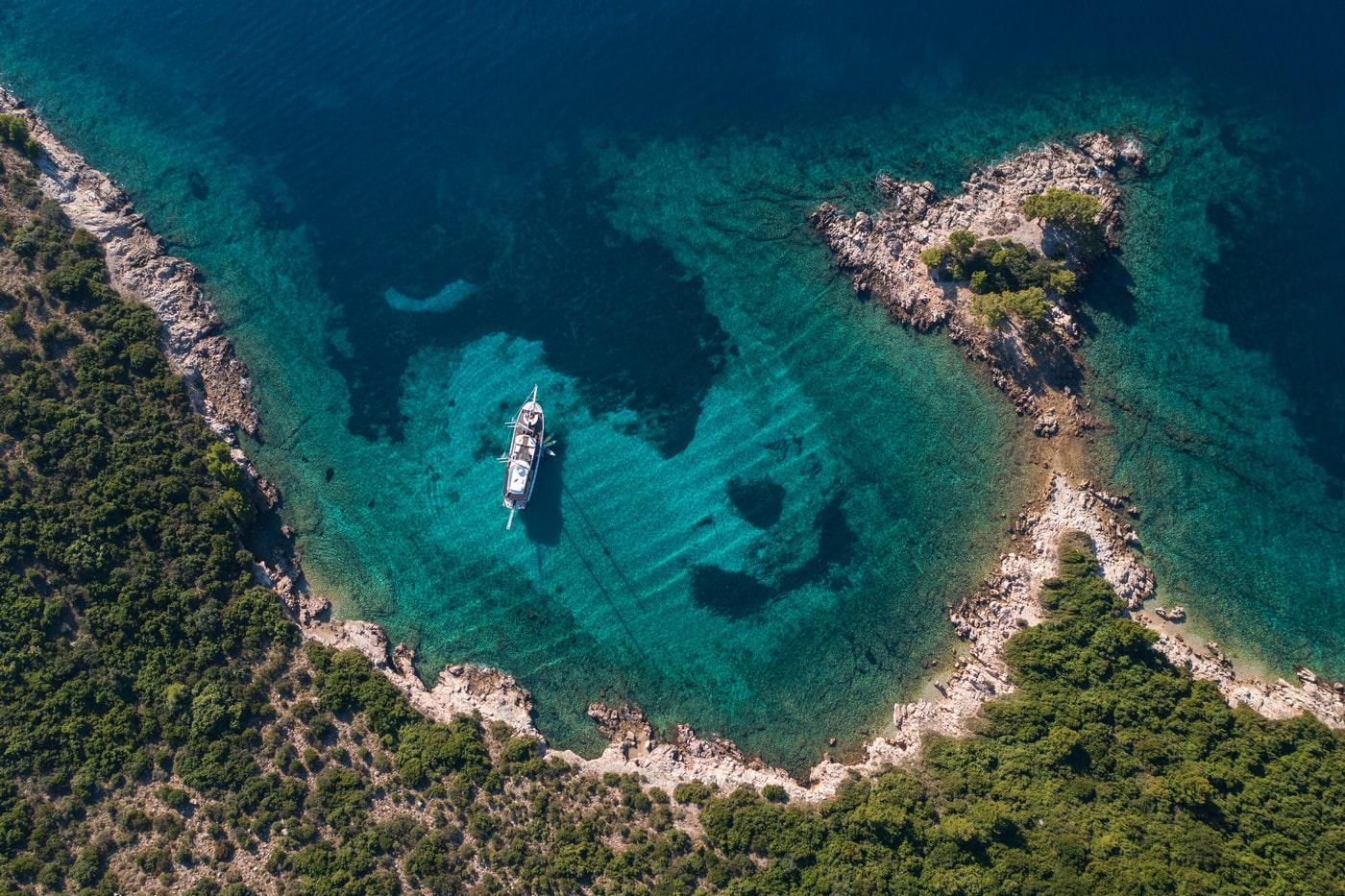 Aerial view luxury yacht anchored pristine turquoise Mediterranean bay surrounded rocky coastline