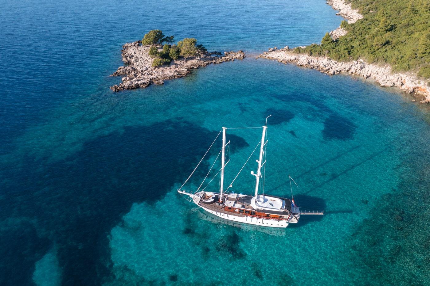 Wooden gulet yacht anchored in crystal clear turquoise waters near rocky coastline