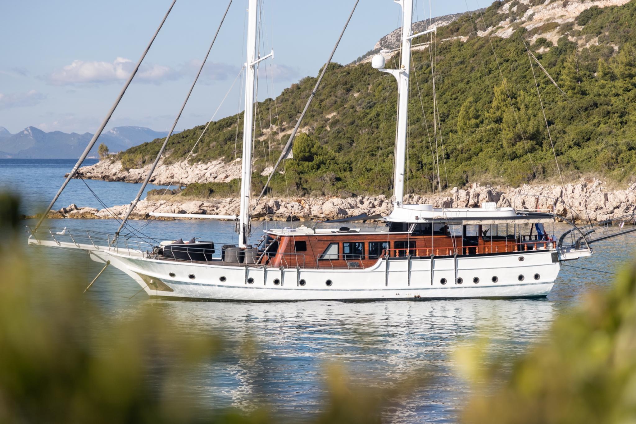 white traditional gulet yacht with wooden superstructure anchored in calm Mediterranean bay with forested coastline
