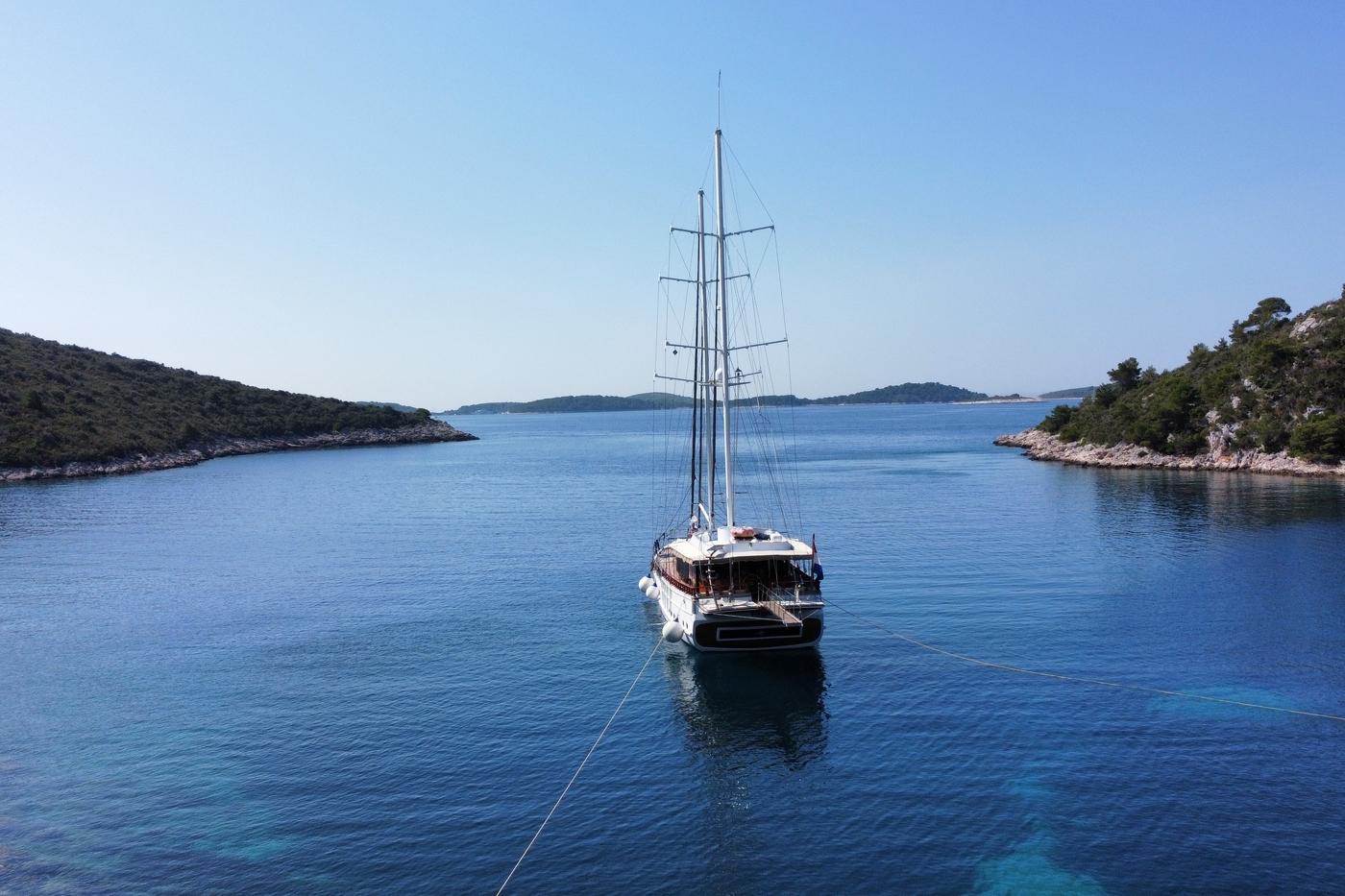white gulet with two masts anchored in crystal blue waters surrounded by forested coastline