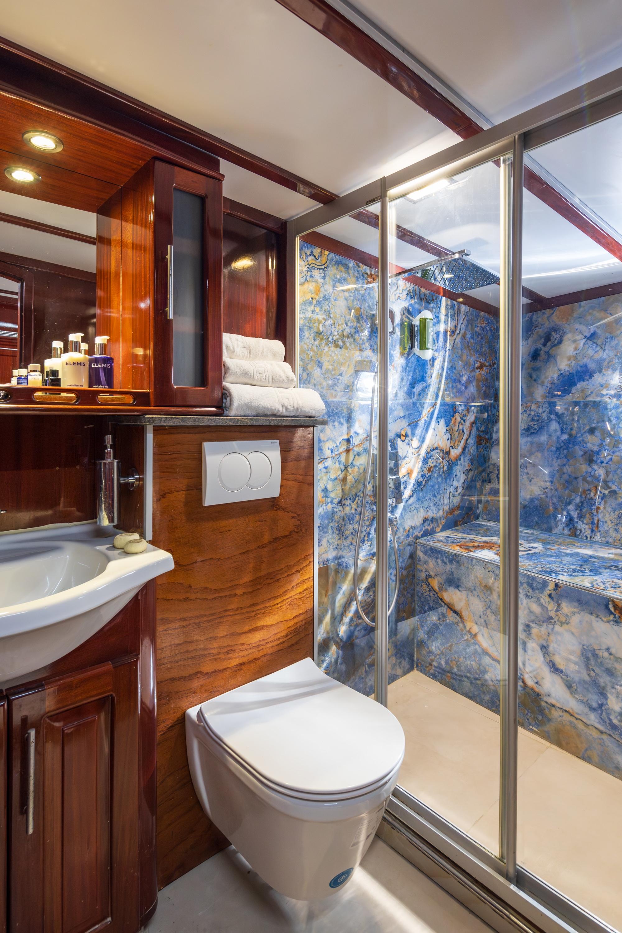 luxury yacht ensuite bathroom featuring blue marble shower enclosure and polished wood cabinetry