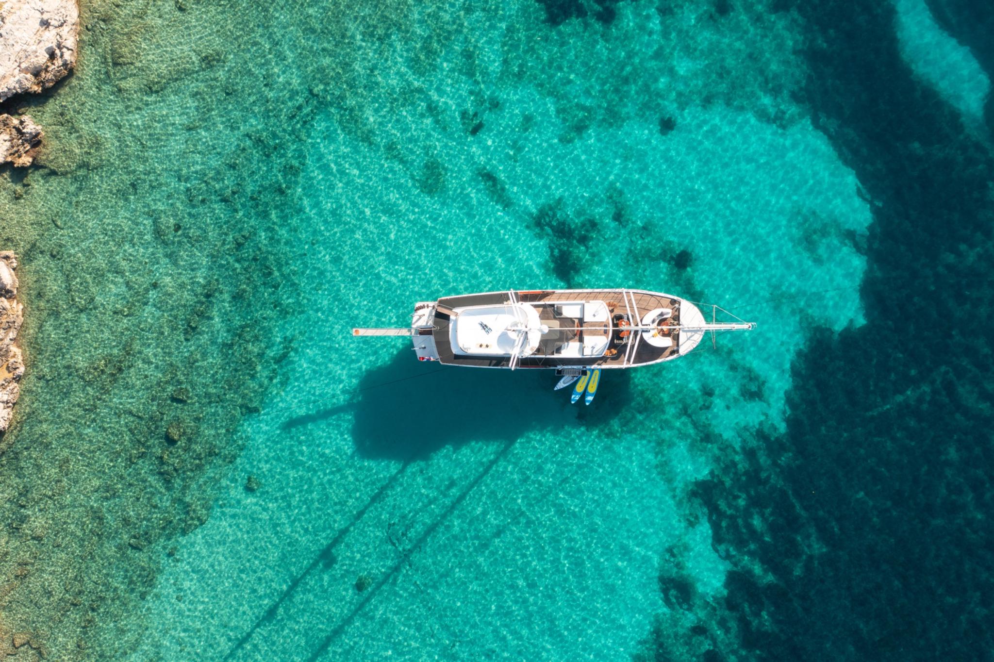 aerial view of white gulet yacht anchored in crystal clear turquoise waters with paddleboards