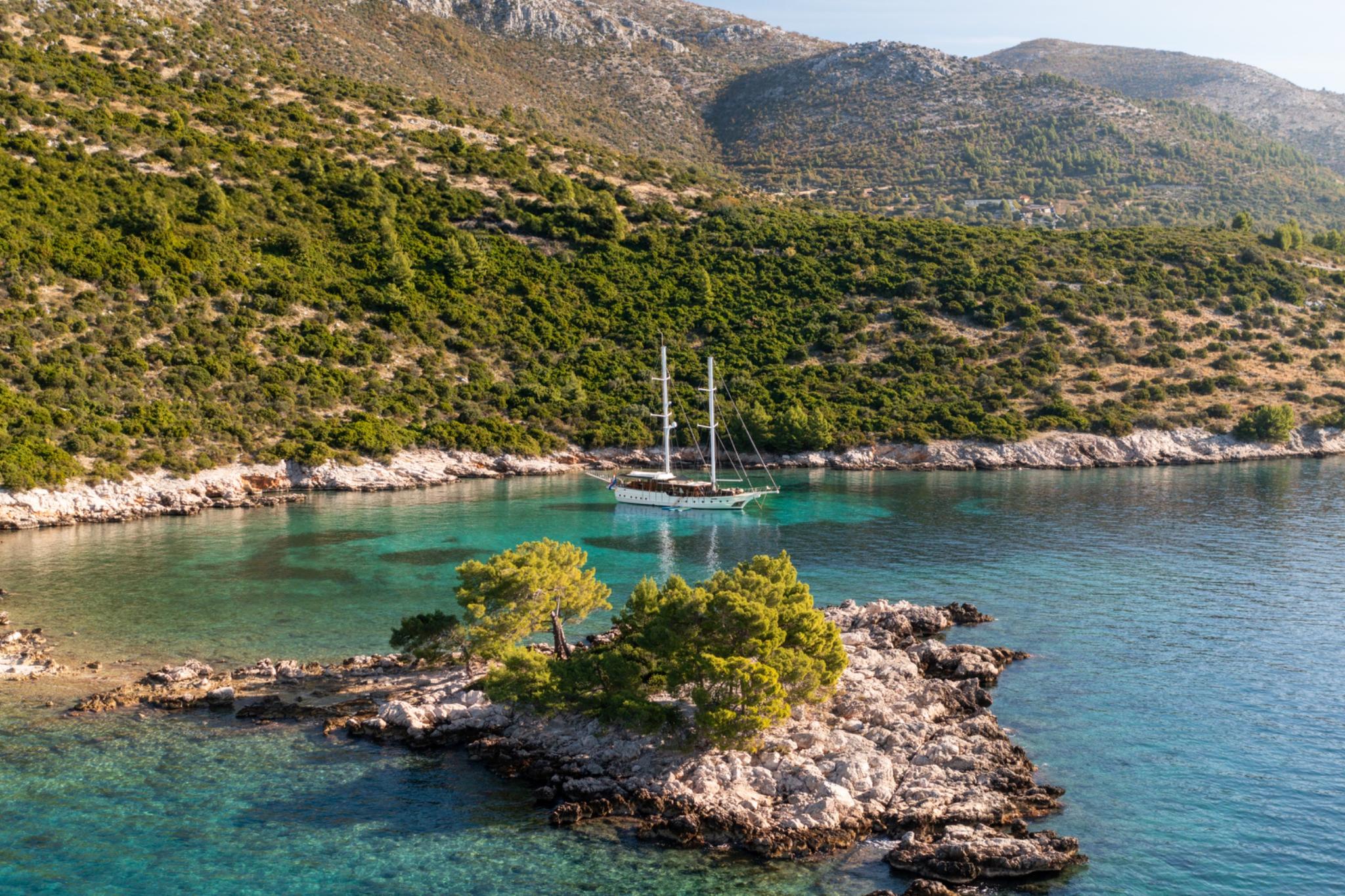 Traditional wooden sailing yacht at anchor in crystal clear turquoise bay surrounded by rocky coastline