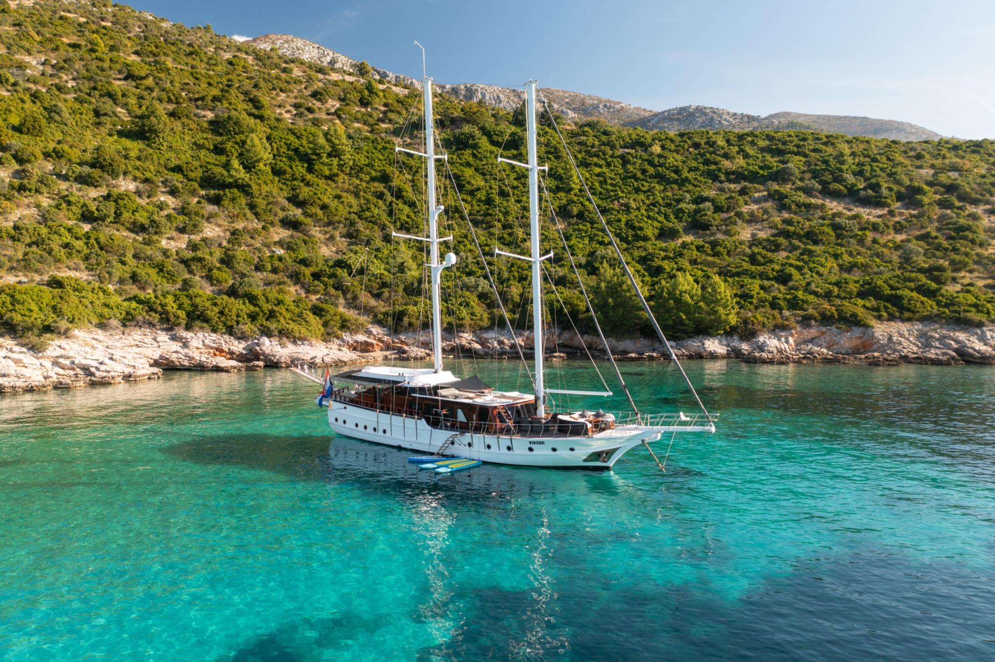 white gulet yacht anchored in crystal clear turquoise waters near forested Mediterranean coastline