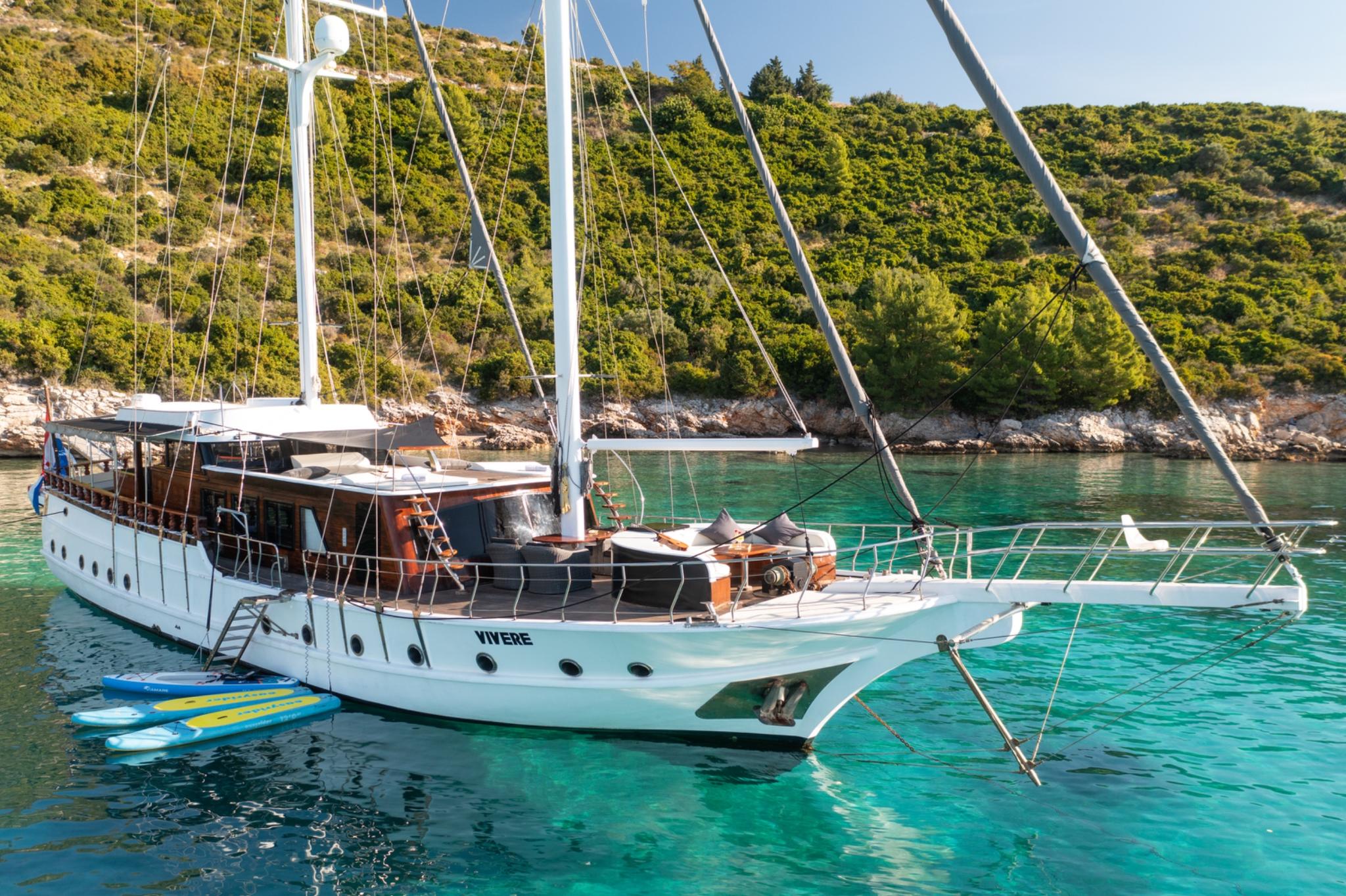 Traditional wooden gulet named Vivere anchored in turquoise bay with inflatable water toys