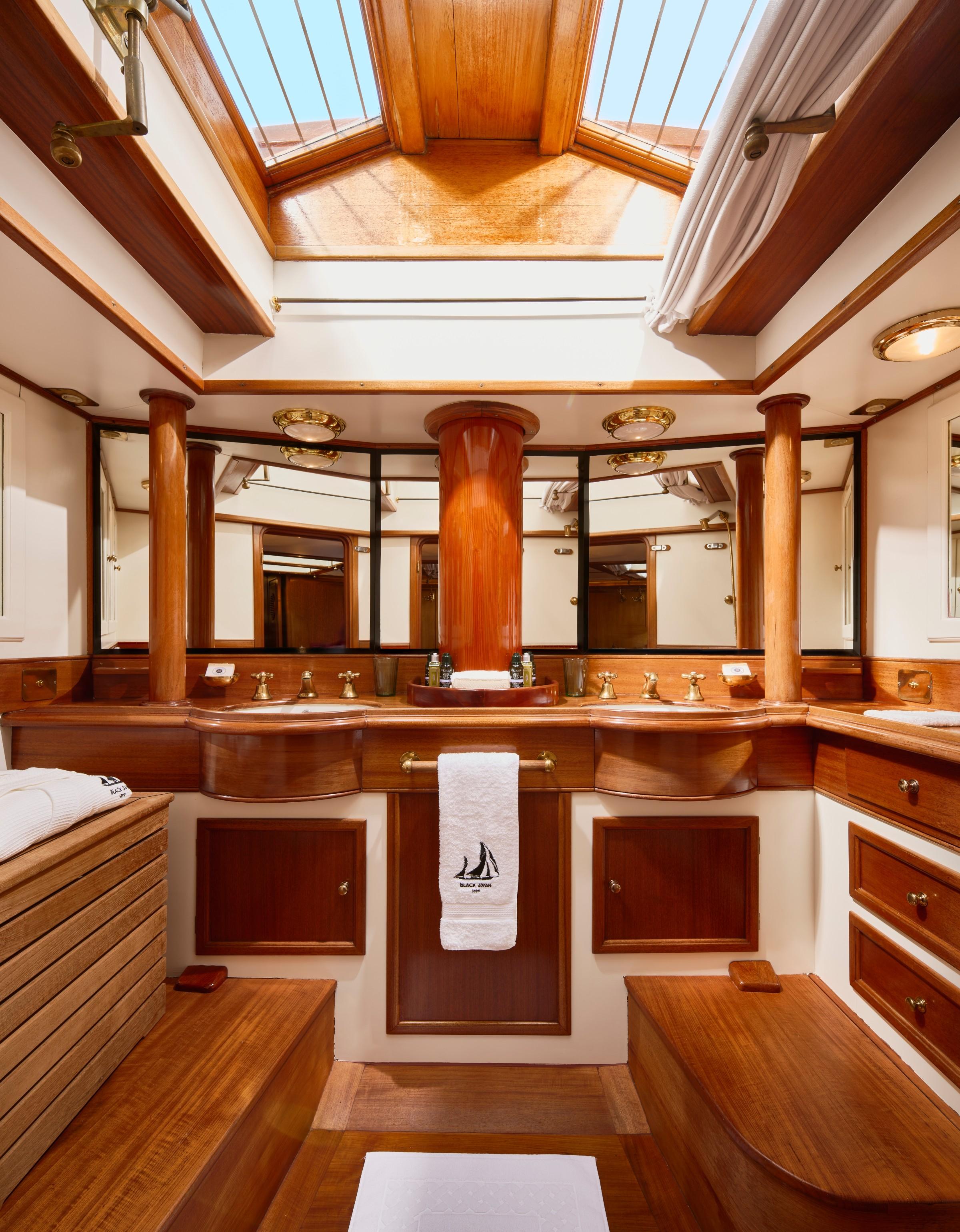 Black Swan gulet master bathroom with twin wooden vanity units, brass fittings, and overhead skylight