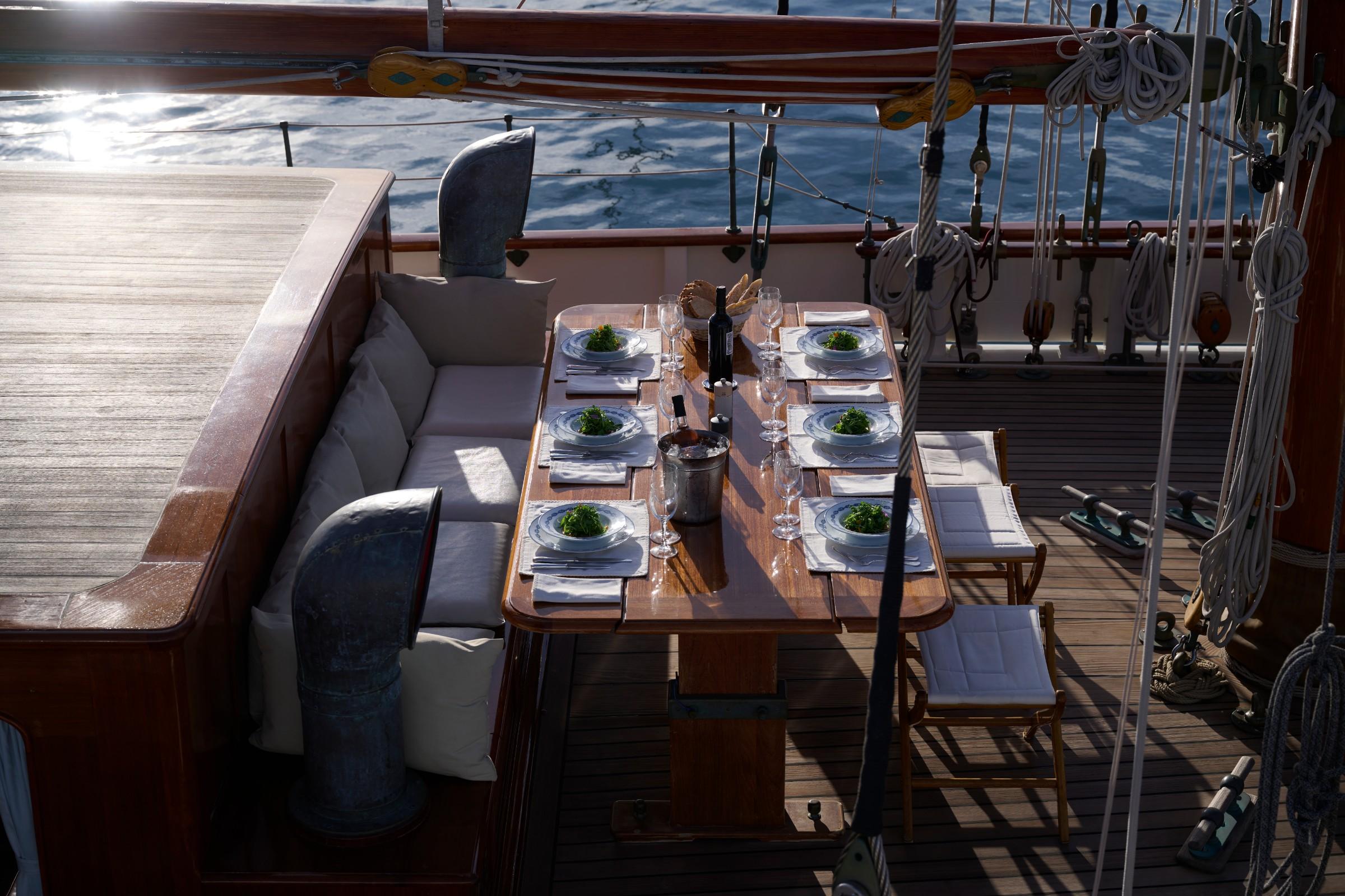 Gulet aft deck dining table set for six with plated salads, wine bottle, champagne bucket and crystal glasses at sea
