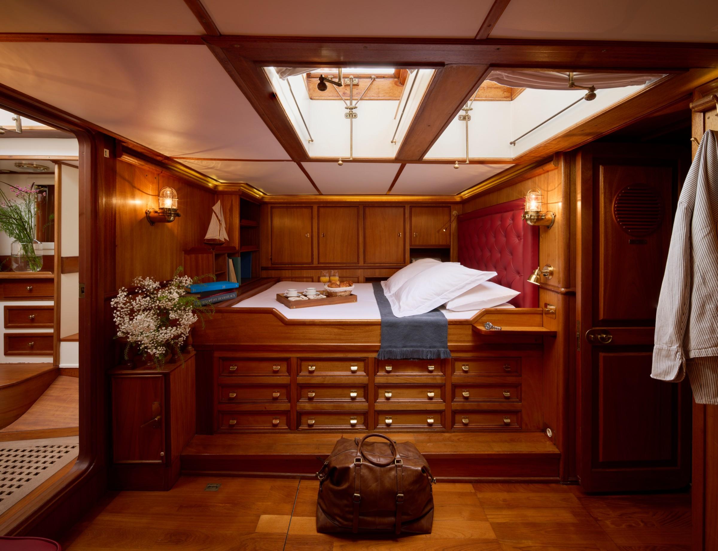 Gulet master cabin with tufted red headboard, raised double bed, brass fittings, and overhead skylight hatch