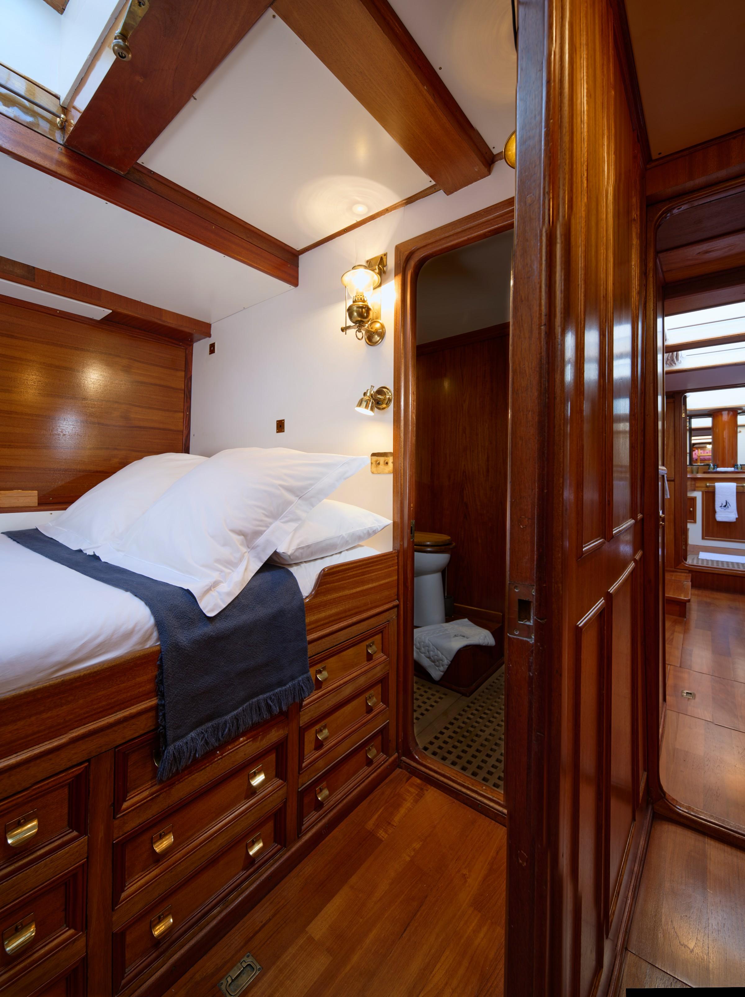 Gulet guest cabin with double bed, brass fittings, built-in mahogany drawers, and en-suite WC visible through open door