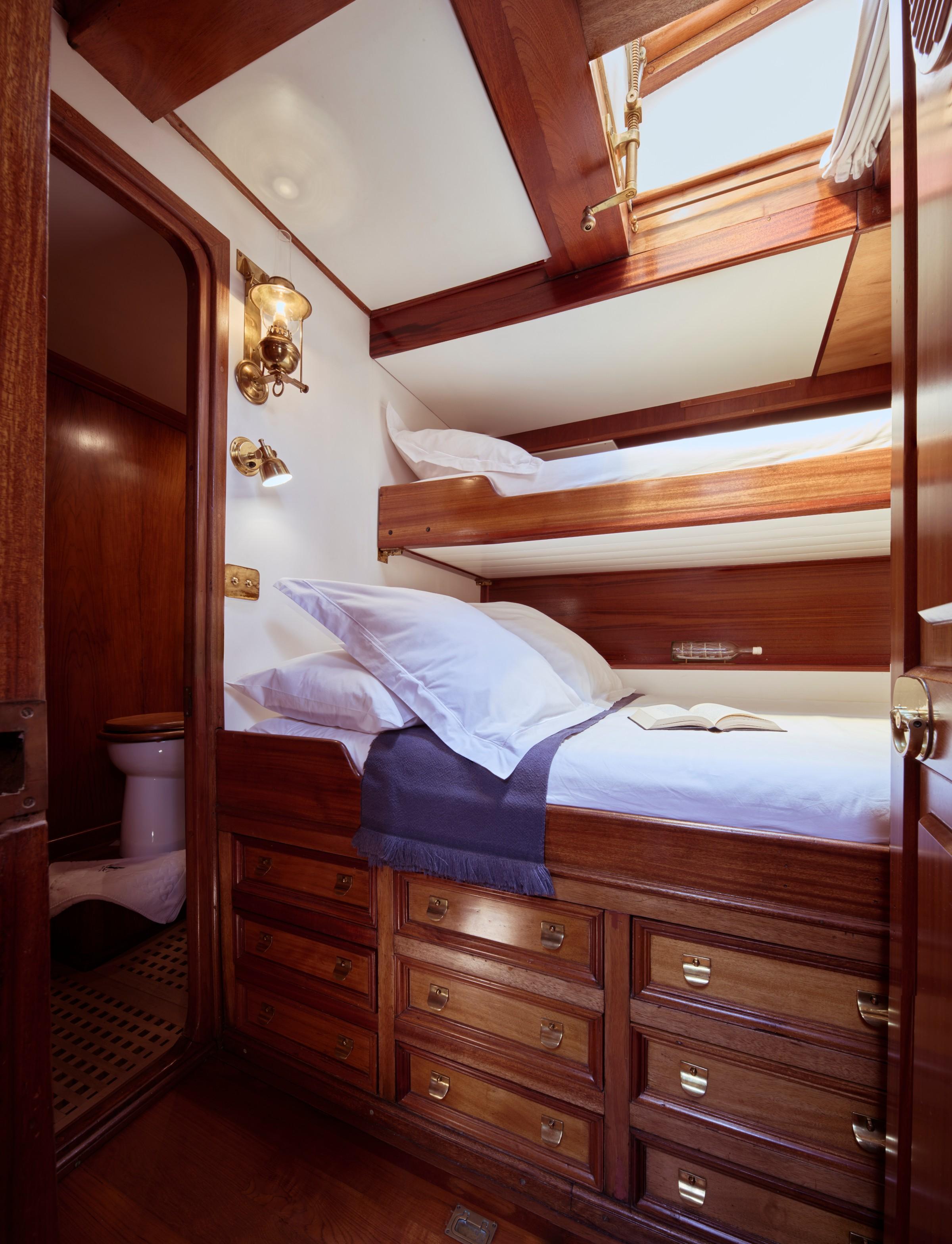 twin bunk cabin with rich mahogany woodwork, brass fittings, built-in storage drawers, and en-suite toilet visible through doorway