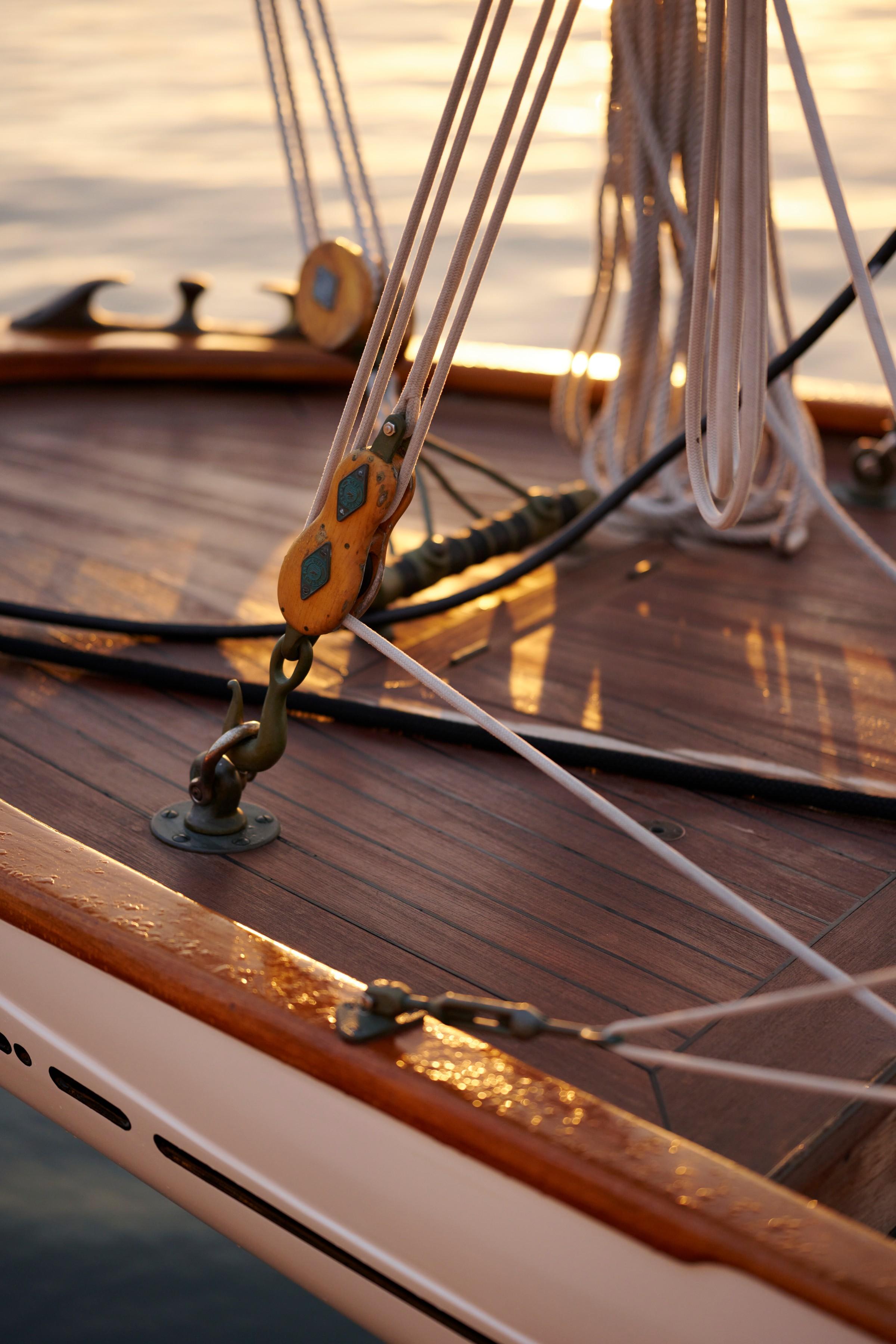 Traditional wooden gulet deck with brass block and tackle pulley, white ropes, and teak planking at golden sunset