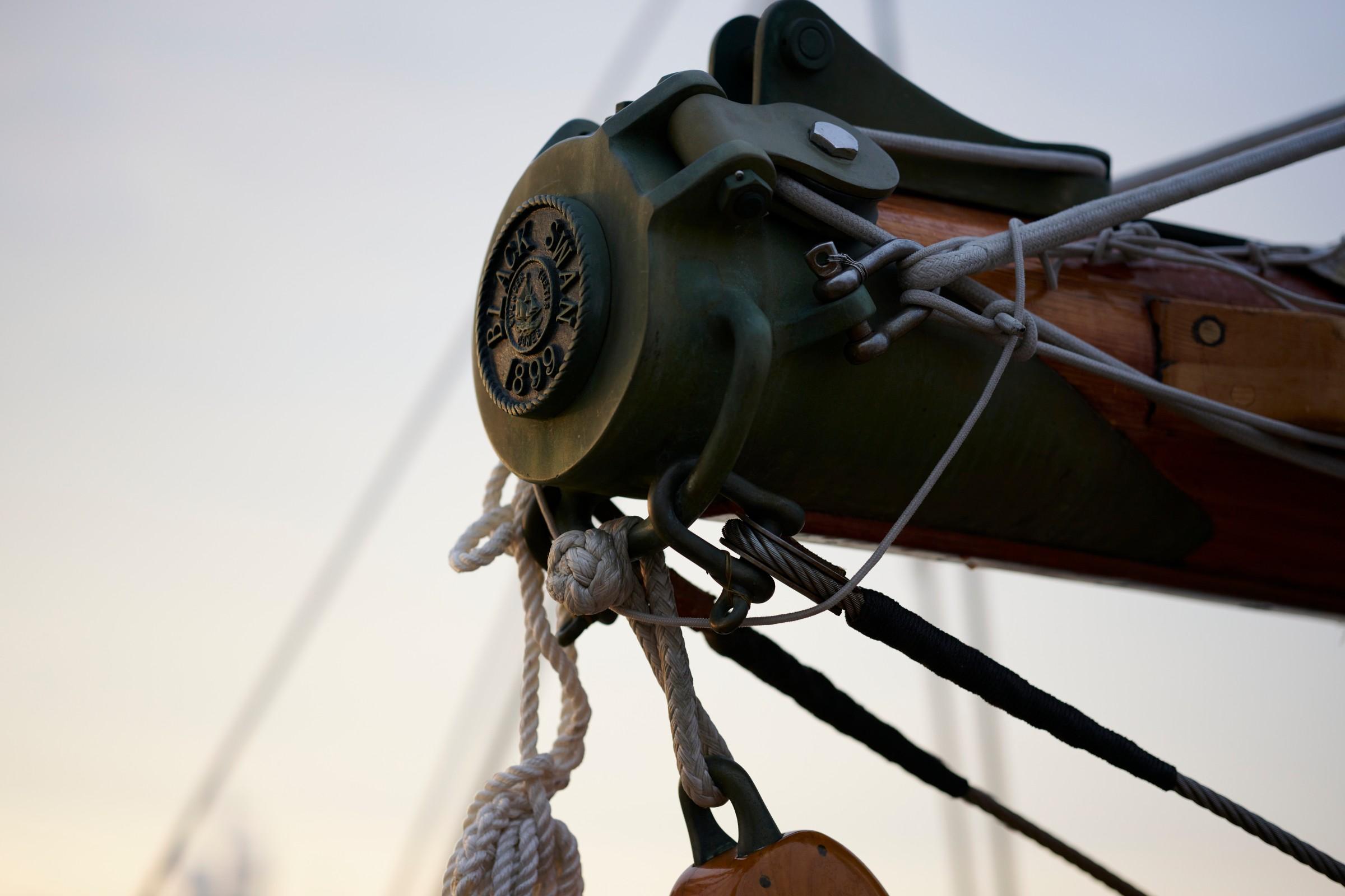 Close-up of Black Swan 899 bronze medallion on dark green bowsprit cap with knotted ropes and rigging at dusk