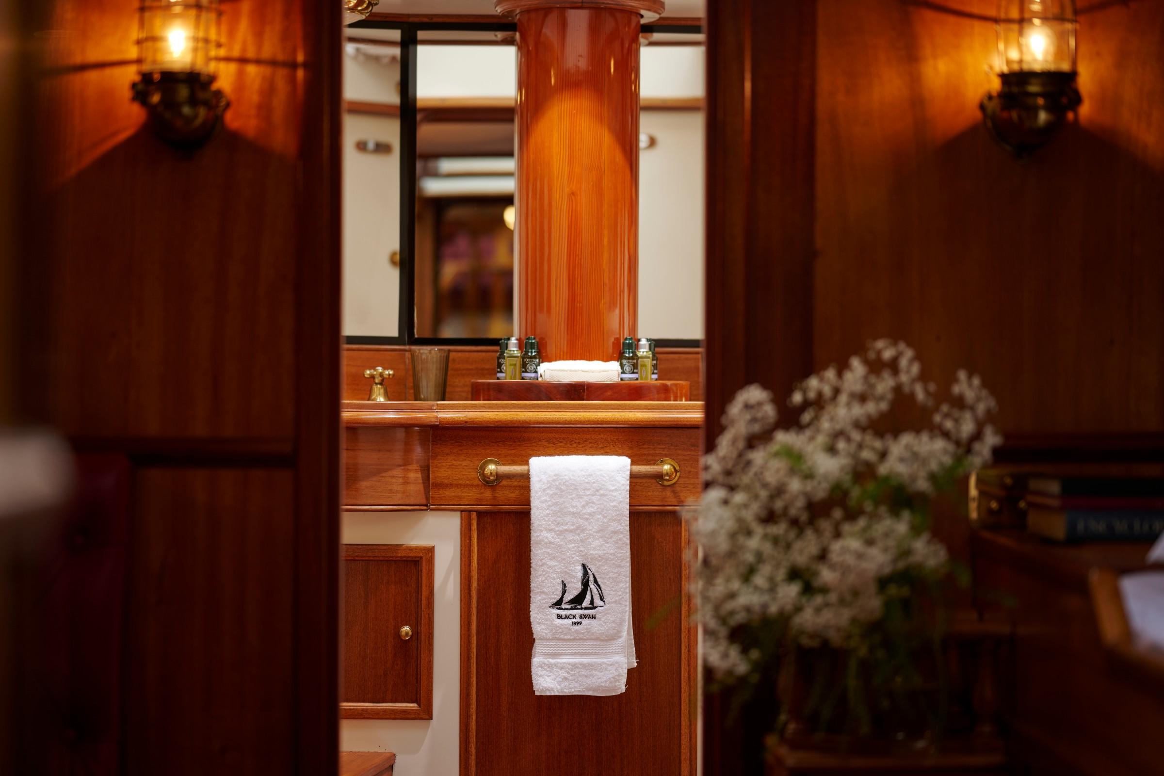 Luxury gulet cabin bathroom with mahogany woodwork, brass fittings, and Black Swan embroidered towel