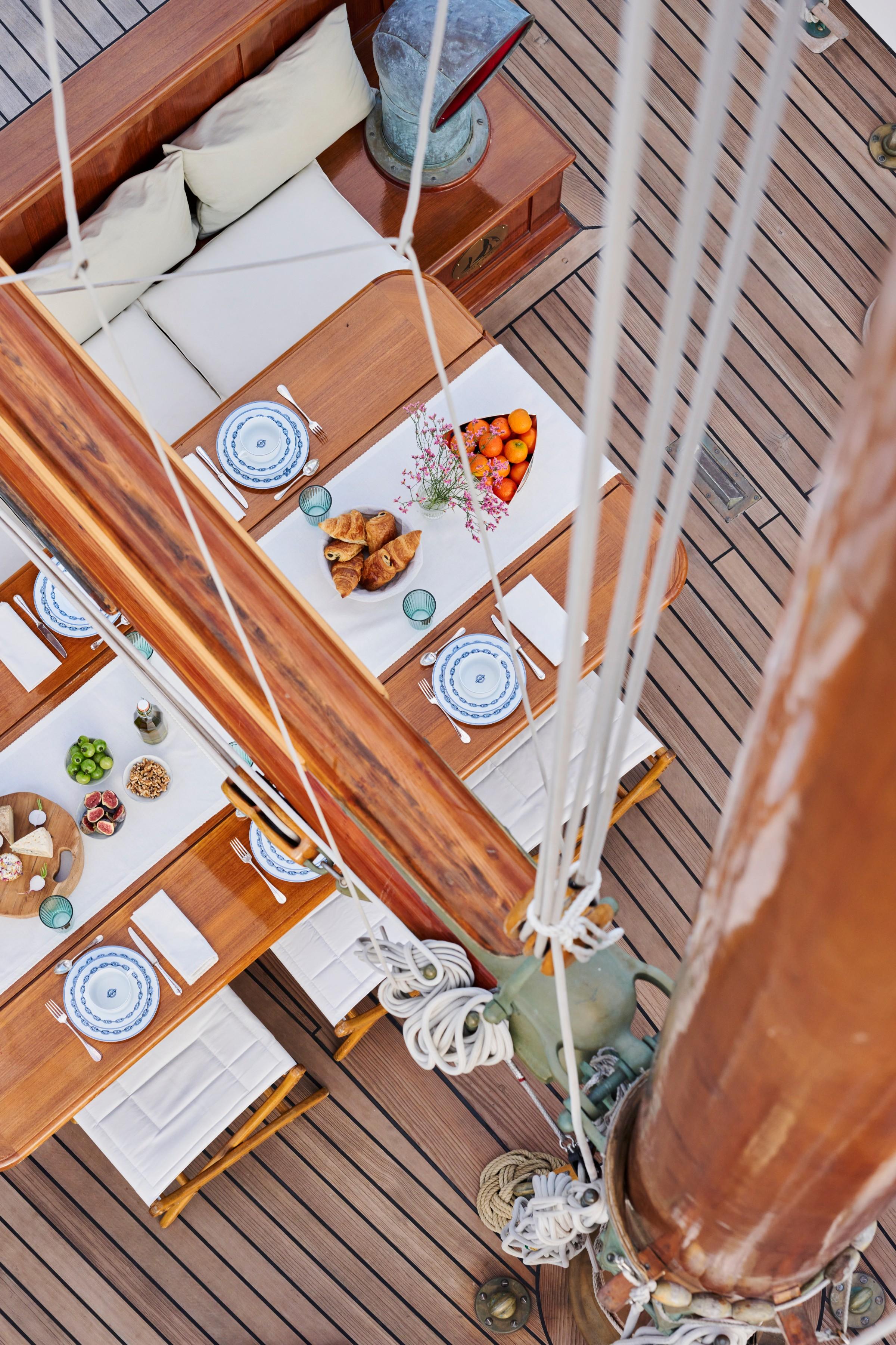 Aerial view of gulet deck dining table set with blue and white crockery, croissants, fresh oranges, figs and flowers