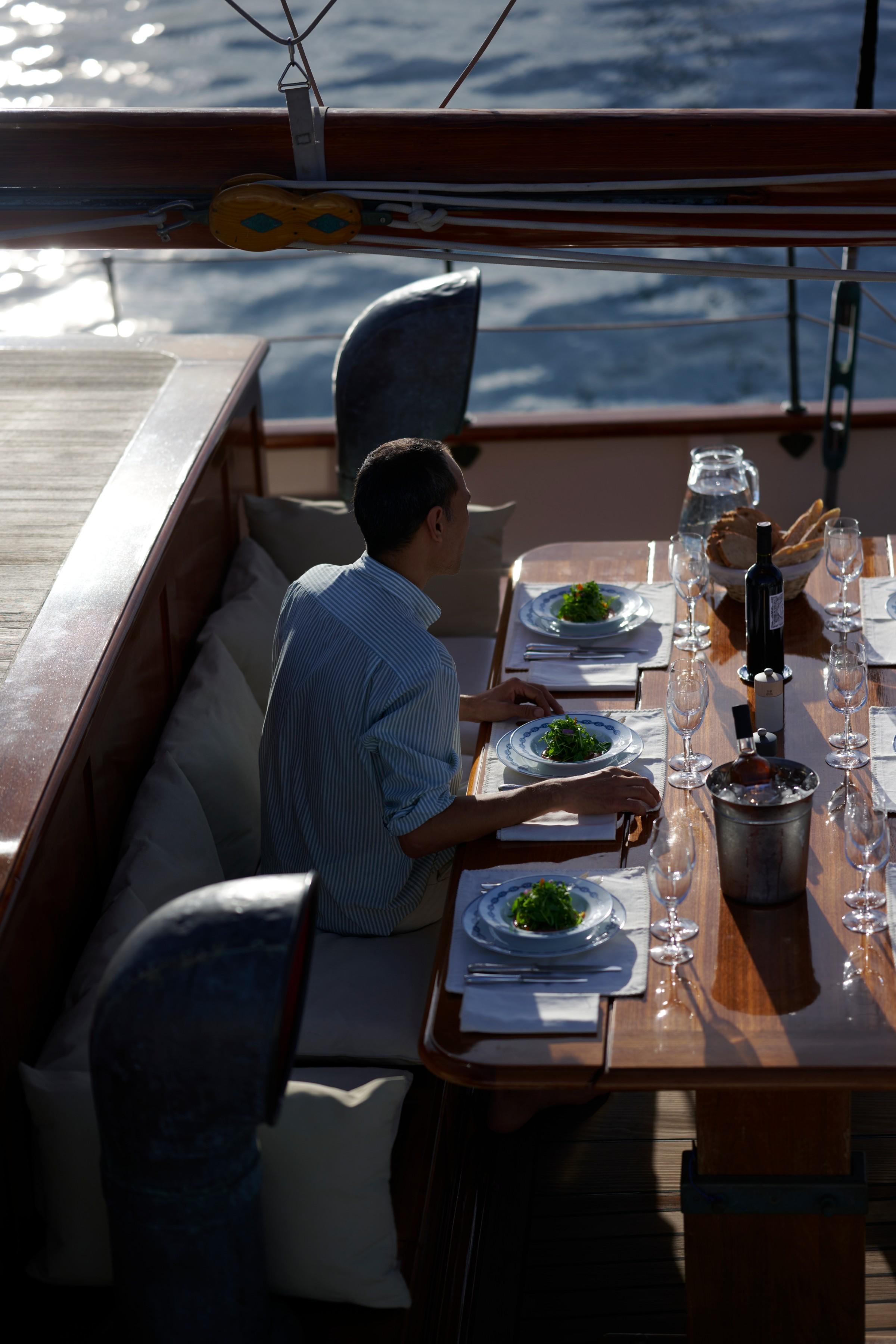 crew member serving fresh salad starters at a formally set teak dining table on gulet aft deck with wine bottle in ice bucket and sparkling sea behind