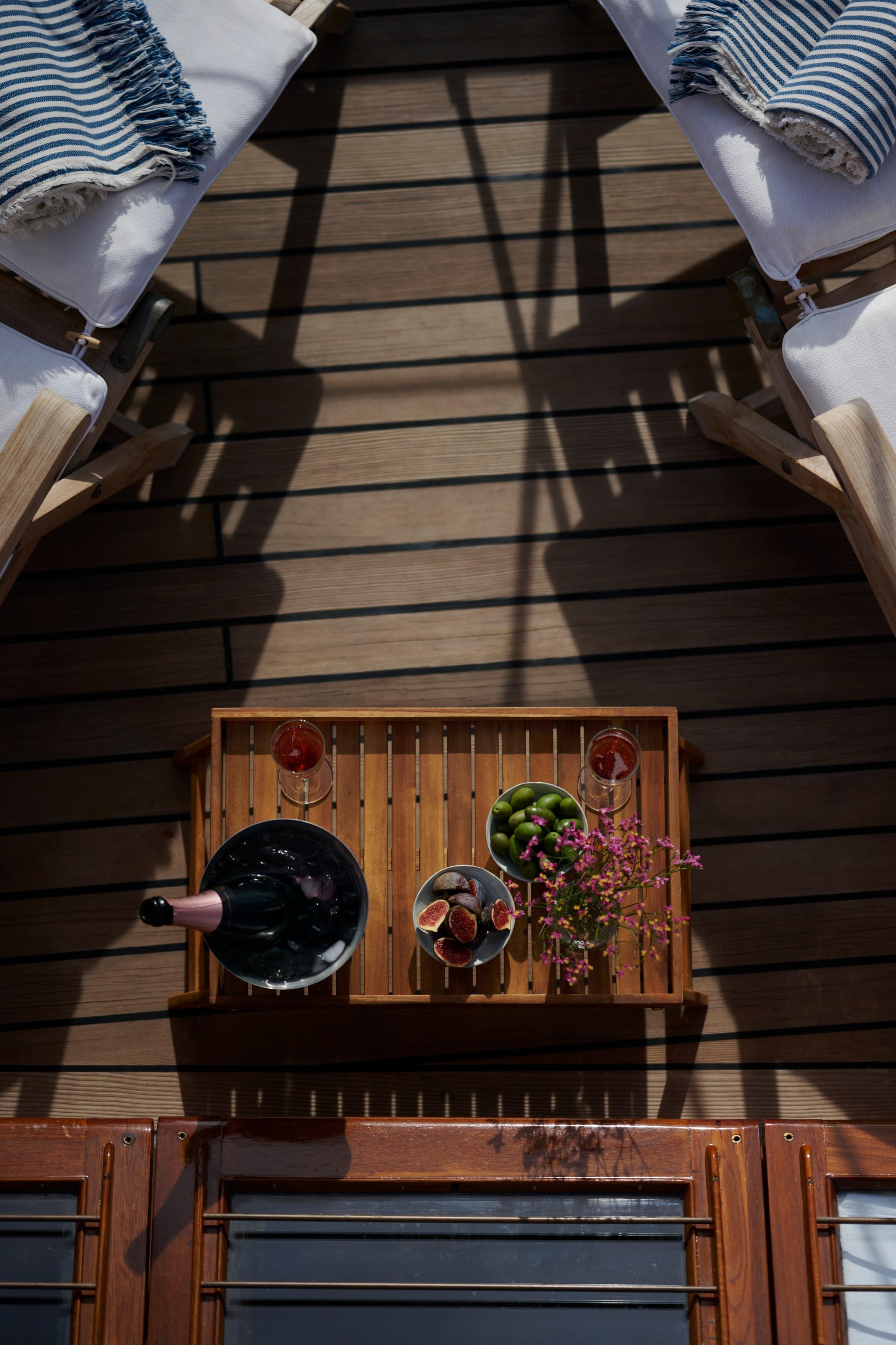 overhead view of gulet sun deck tray with champagne on ice, fresh figs, green olives, wine glasses and pink flowers between two sun loungers
