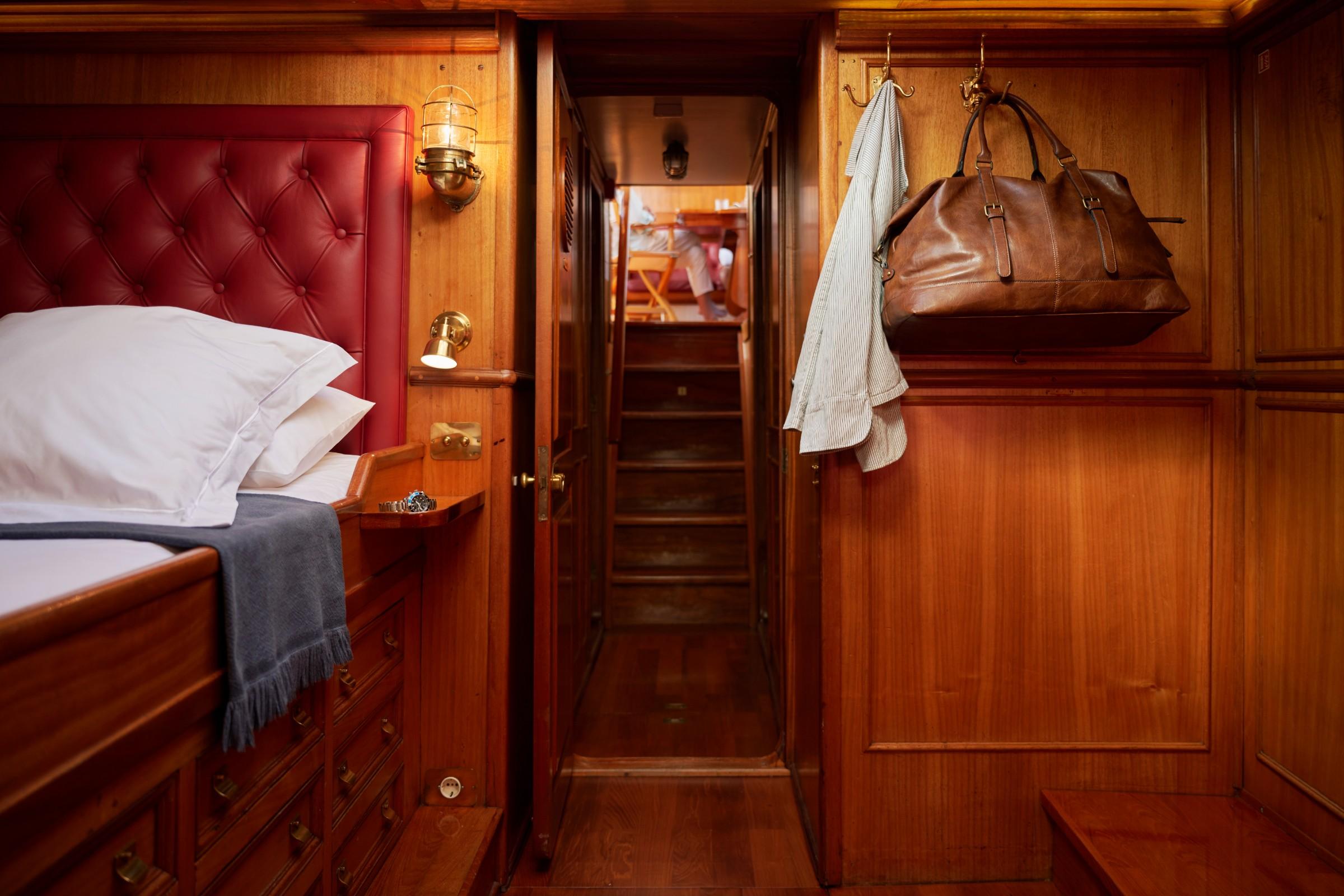 Gulet cabin with red button-tufted leather headboard, warm mahogany panelling, brass fittings, and companionway stairs leading to deck above