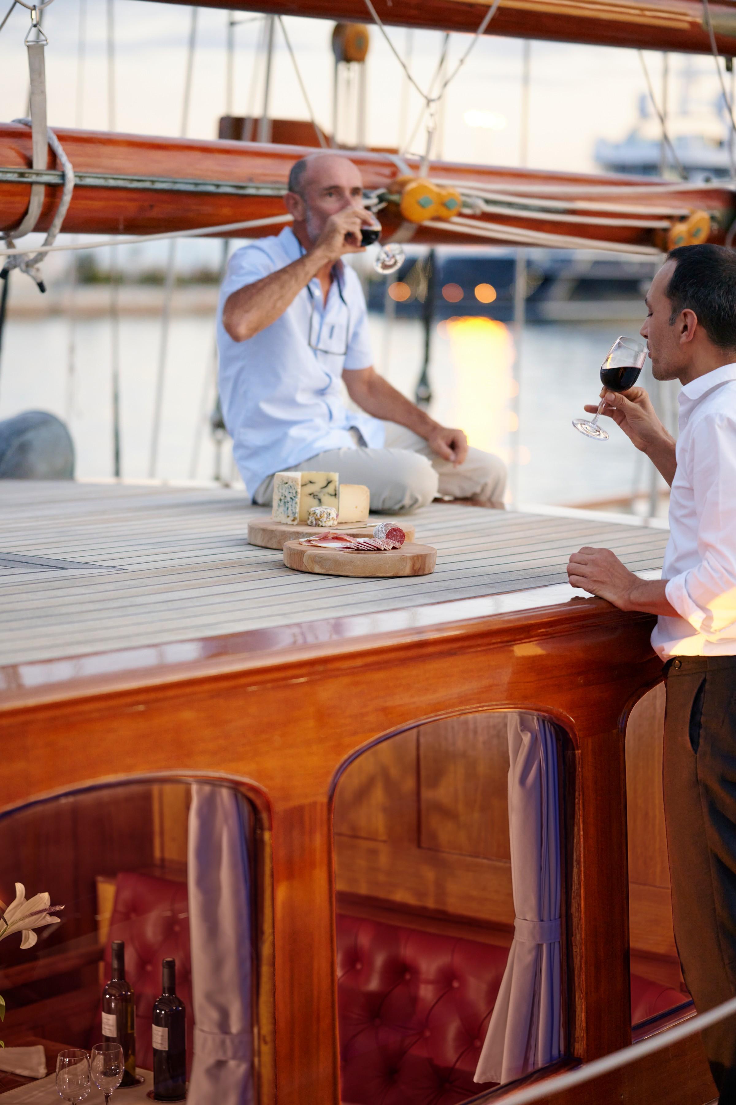 two guests drinking red wine with cheese and charcuterie board on gulet deck at sunset